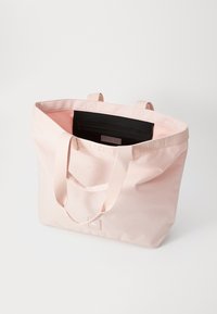 Borsa tote Lacoste rosa chiaro con doppie maniglie e tasca interna zip nera visibile su sfondo bianco.