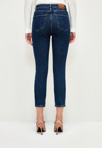 Tmavě modré slim-fit džíny mají pět kapes, rovný střih nohavic a hnědou koženou nášivku na zadním pásku.