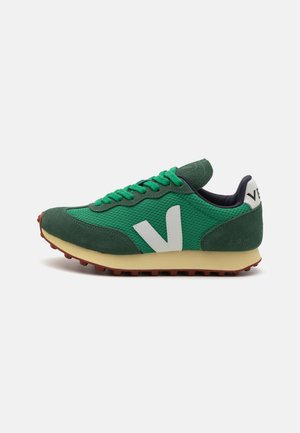 Green athletic shoe with mesh and suede materials, white logo, contrasting rubber sole, and lace-up design. Features a tab on the heel.