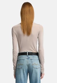 Lys beige langærmet top parret med slidte blå denimjeans, der har et sort bælte og gule zigzag-syninger på baglommerne.