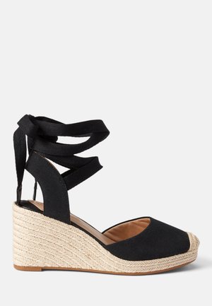 Kileformet espadrillesandal med sort stofoverdel, ankelbind og naturligt flettet jute-platformhæle.