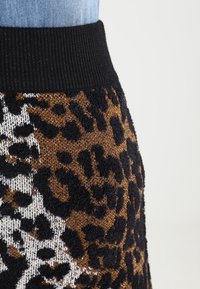 Virkat kjol med leopardmönster i brunt och svart, med en svart ribbad midja. Mjuk textur med kontrasterande mönster.