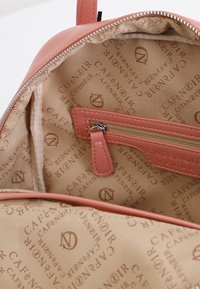 Interiér růžového batohu z jemného růžového odstínu obsahuje hladkou koženou kapsu na zip a béžové podšívání s opakovaným logem "CAFÉ NOIR".