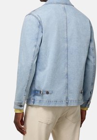 Vaaleansinisestä denimmateriaalista valmistettu takki, jossa on klassinen muotoilu, leveä kaulus, napilliset kalvosimet ja kaksi säädettävää takataskua.