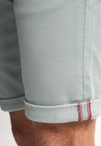 Pantaloni shorts in cotone grigio chiaro con orlo a risvolto e cuciture di accento rosse. Texture liscia e design sartoriale visibile sulla gamba.