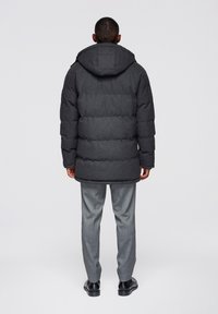 Grå vadderad jacka med huva, med en quiltad textur och en avslappnad passform, kombinerad med ljusgrå byxor och svarta skor.