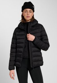 Czarna kurtka puchowa z kapturem, z pikowanym wzorem, zamkiem błyskawicznym z przodu i elastycznymi mankietami. Nosi się ją na czarną bluzkę i legginsy.