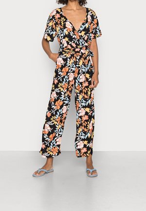 Combinaison fleurie à base noire, ornée de fleurs orange, rose et bleu clair. Col en V, manches courtes, taille nouée et coupe à jambes larges.