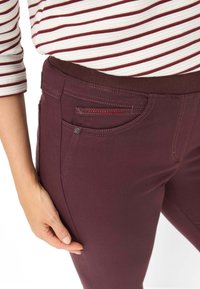 Bordeauxkleurige jeans met een aansluitend ontwerp, elastische taille en een klein zakje met rode stiksels, gemaakt van een zachte katoenmix.