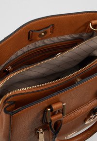 Sac à main en cuir brun texturé avec ferrures dorées. L'intérieur comprend plusieurs compartiments doublés de tissu matelassé beige et fermés par des fermetures éclair.