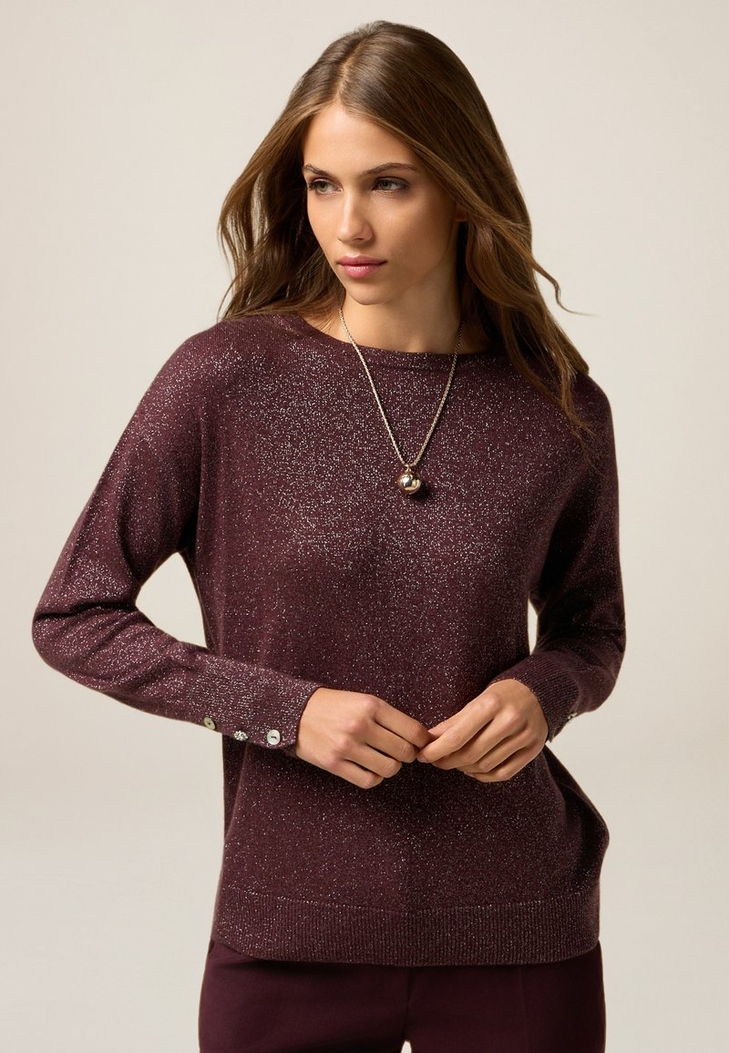 Maglione bordeaux con una morbida texture scintillante. Presenta maniche lunghe e dettagli in bottone sui polsi. Collo a giro, vestibilità morbida.