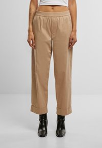 Pantaloni leggeri beige con vita elastica, gambe larghe e orli arrotolati, abbinati a stivaletti neri. Texture liscia.