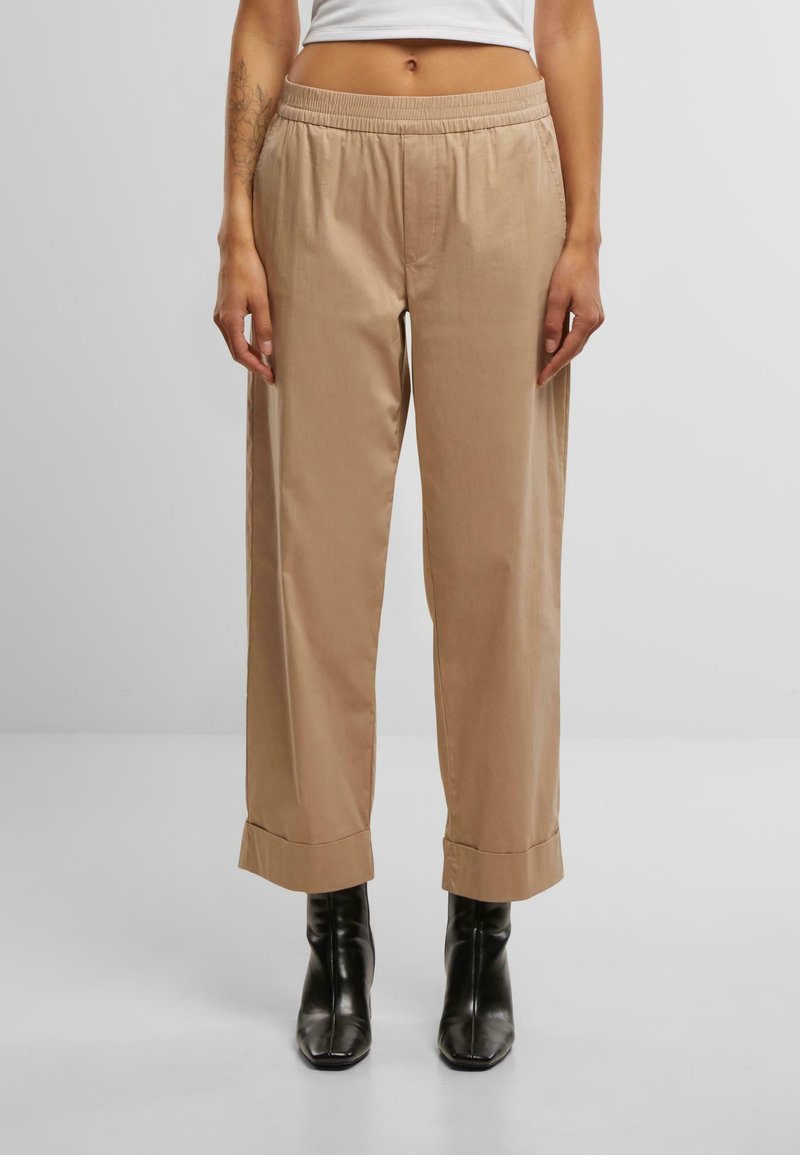 Pantaloni leggeri beige con vita elastica, gambe larghe e orli arrotolati, abbinati a stivaletti neri. Texture liscia.