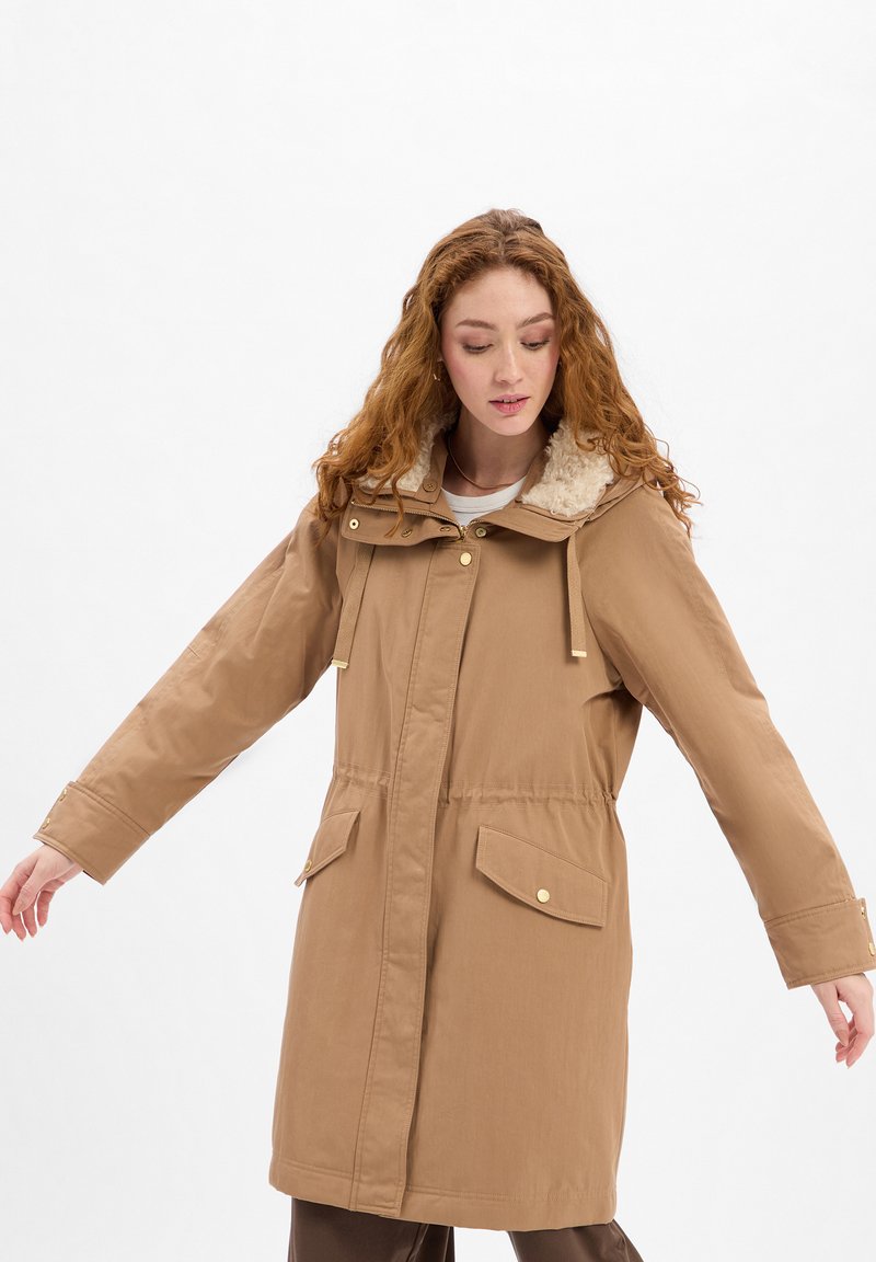 Brown, mid-length parka with a removable fur-lined hood, front pockets, and gold hardware accents; smooth, water-resistant fabric.