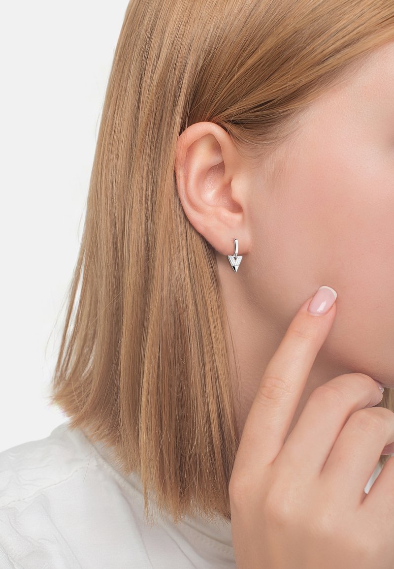 Orecchini triangolari in argento presentano un design pulito con una finitura lucida e un accento sulla punta, mostrati all'orecchio di una modella.