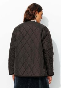 Veste matelassée noire avec un motif en diamant, manches longues et ourlet arrondi. Fabriquée en matériau lisse avec un design léger.