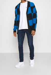 Blå och svart rutigt mönster kofta i fluffigt tyg, över en vit t-shirt, tillsammans med mörkblå jeans och vita sneakers.