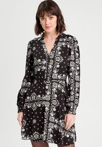 Robe noire avec des motifs floraux blancs, fermeture à boutons sur le devant et longues manches bouffantes. Présente un corsage ajusté et une jupe évasée. Tissu léger.