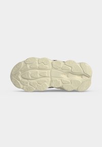 Semelle d'une basket beige avec des motifs ovales et ondulés texturés et irréguliers pour l'adhérence et la flexibilité sur un fond uni.