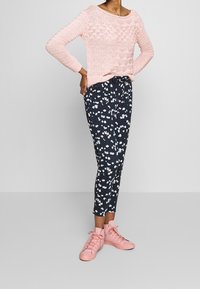 Ljusrosa stickad tröja med texturerat mönster, i kombination med marinblå blommiga byxor och rosa högskor.