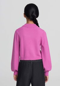Pullover rosa corto con scollatura ampia e maniche a sbuffo, realizzato in tessuto morbido, abbinato a pantaloni neri a vita alta.