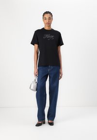 Black short-sleeve t-shirt featuring a silver embroidered logo, paired with blue wide-leg denim jeans and black pointed heels, holding a silver bag.