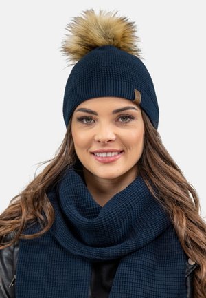 Navy knit beanie with a faux fur pom-pom on top. The accompanying scarf features a textured, ribbed design, also in navy.