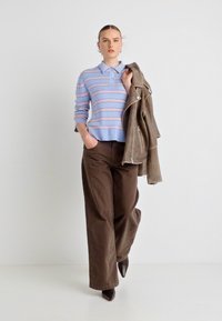 Ριγέ μπλε και ροζ πόλο μπλουζάκι με στρώση από καφέ σατέν μπουφάν, συνδυασμένο με φαρδιά καφέ παντελόνια και αιχμηρές μαύρες γόβες.