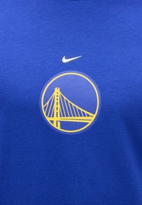 Μπλε ύφασμα με κίτρινο λογότυπο Golden Gate Bridge μέσα σε κύκλο κάτω από το λευκό σύμβολο Nike swoosh.