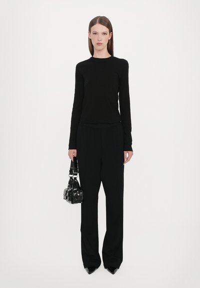 Maglietta nera a maniche lunghe e pantaloni larghi su misura, abbinati a una piccola borsa nera. Tutti gli articoli sono di un nero uniforme, caratterizzati da materiali eleganti.