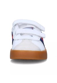 Baskets blanches avec des bandes Velcro, semelle en gomme, et un panneau latéral en textile coloré arborant un motif rouge et bleu. Matériaux lisses et texturés.