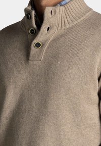 Beige gebreide trui met een hoge kraag, voorzien van een drieknoopsluiting, geribbelde halslijn en een subtiele textuurdesign.