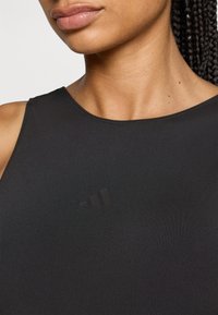 Schwarzes sportliches Tanktop mit rundem Ausschnitt und dünnen Trägern. Mit einem dezenten schwarzen Logo im Brustbereich. Glatte Stofftextur.