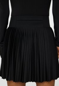 Musta korkeavyötäröinen laskostettu hame, jota on yhdistetty mustaan pitkähiharaiseen paitaan, keskittyen vyötäröön ja reiden yläosaan.