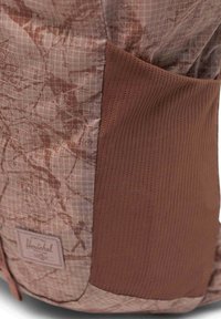 Sac à dos Herschel en tissu à motif brun avec texture en grille, complété par une poche latérale en maille brun uni et un patch de logo.