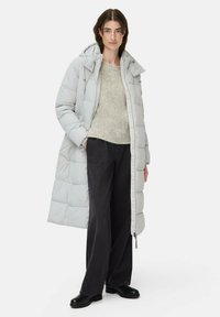 Lys grå pufferjakke med hætte, quiltet design og frontlynlås, kombineret med en struktureret beige sweater og sorte vide bukser.