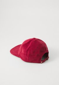 Casquette de baseball en velours côtelé rouge avec une visière courbée, tissu texturé, sangle ajustable à l'arrière et deux œillets de ventilation sur les côtés.