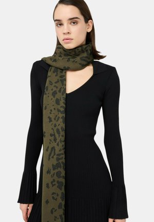 Sciarpa verde oliva con motivo animalier maculato nero, realizzata in materiale morbido, drappeggiata intorno al collo, indossata con un abito nero a maniche lunghe a coste.