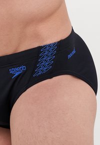 Slip de bain noir avec motif zigzag bleu et logo. Fabriqué en tissu durable, avec une texture lisse et un ajustement confortable.