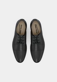 Zapatos formales de cuero negro con cordones, diseño de puntera cerrada, vistos desde arriba sobre un fondo blanco.
