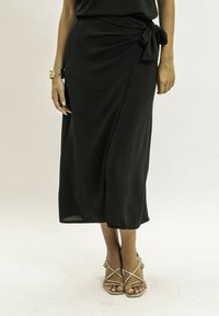 Jupe midi noire avec un nœud à la taille. Fabriquée en tissu léger, elle présente une texture lisse et une silhouette fluide.