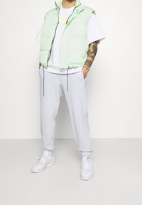 Mentolový pufovaný vest s bílým tričkem, v kombinaci se světle šedými tepláky a bílými teniskami. Mezi vlastnosti patří elastické lemy a kapsy na zip.