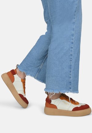 Weiße, orange und rote Sneaker mit oberer Struktur; ausgestattet mit braunen Gummisohlen. Getragen mit hellblauen, ausgefransten Jeans.