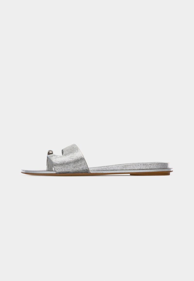 Επίπεδη ασημί μεταλλική σαγιονάρα με μία φαρδιά λωρίδα και θηλιά για τα δάχτυλα, σε ανοιχτό καφέ σόλα, απεικονιζόμενη από το πλάι σε λευκό φόντο.