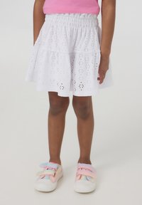 Gonna bianca a strati con motivi ad occhio ricamati, vita elasticizzata arricciata, abbinata a sneakers pastello multicolori con chiusure a strappo.