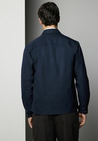 Navy blue shirt with a collar, long sleeves, buttoned cuffs, and a smooth texture. The back features a yoke and minimal detailing.