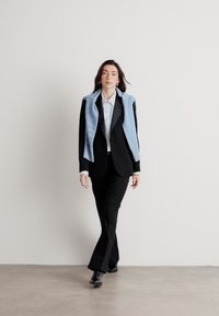 Zwart pak met aansluitende broeken en een op maat gemaakte blazer, gelaagd met een lichtblauwe trui, gecombineerd met een wit shirt en zwarte schoenen.