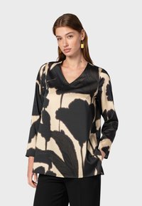 Blusa a motivo nero e beige con scollatura a V, maniche lunghe e motivi a foglia. Tessuto morbido, vestibilità rilassata e design dettagliato.