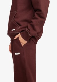 Bordeaux hoodie en bijpassende broek van zachte stof. Voorzien van ribgebreide boorden, zijzakken en contrasterende witte stiksels.