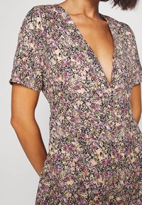 Robe florale avec un décolleté en V profond, manches courtes, fabriquée en tissu léger avec un motif multicolore de roses et de vignes.